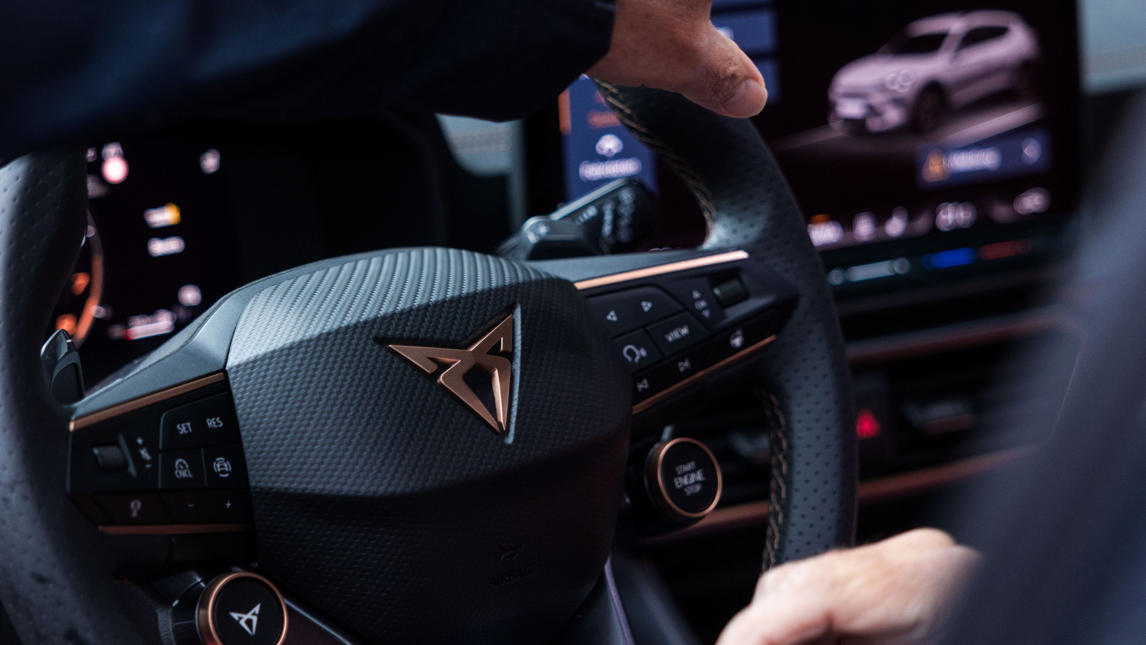 CUPRA Lenkrad mit Hand welche auf den Display im Hintergrund zeigt