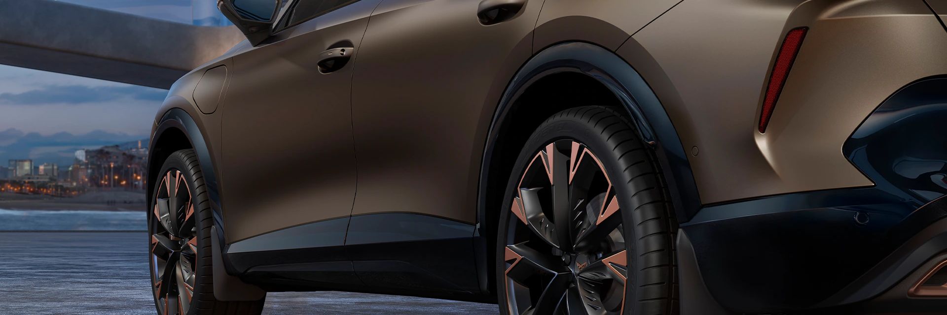 Ein CUPRA Formentor in einer Garage, mit Detailansicht auf die Hinterräder und Schmutzfänger. Das Fahrzeug ist in Bronze lackiert. Im Hintergrund sind architektonische Strukturen und eine Stadtlandschaft bei Dämmerung zu sehen.