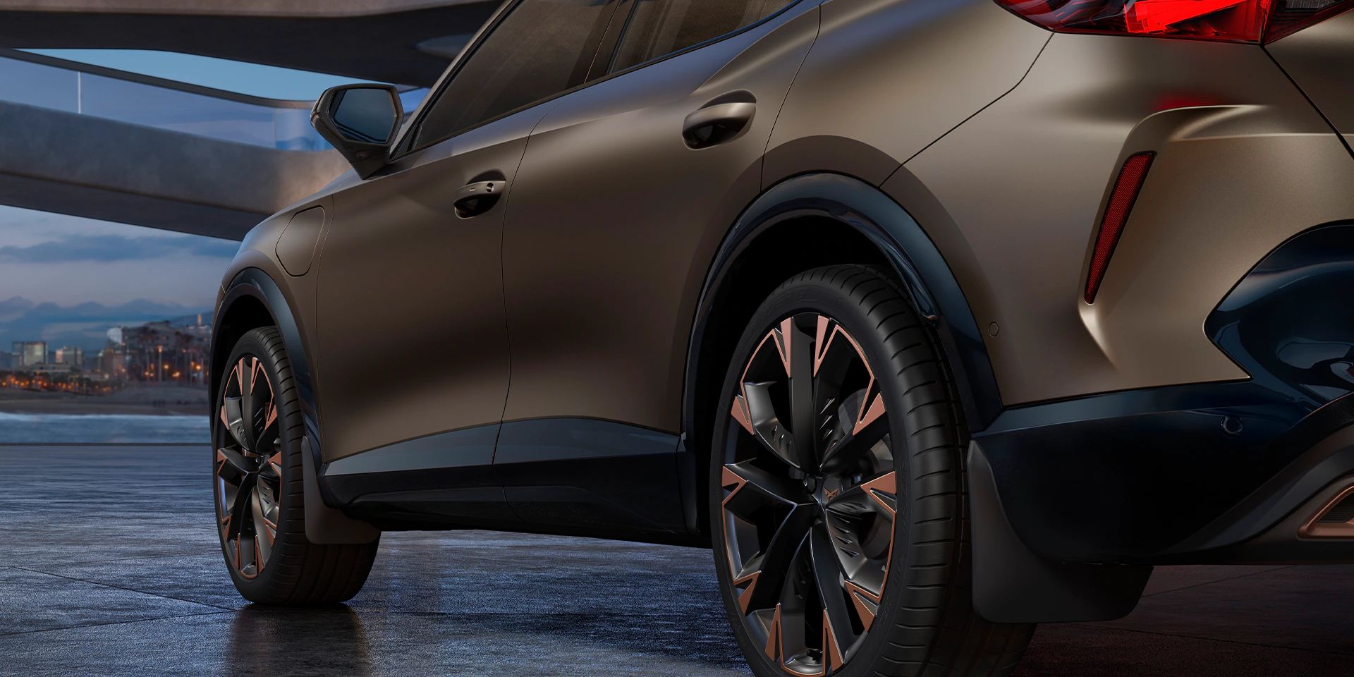 Ein CUPRA Formentor in einer Garage, mit Detailansicht auf die Hinterräder und Schmutzfänger. Das Fahrzeug ist in Bronze lackiert. Im Hintergrund sind architektonische Strukturen und eine Stadtlandschaft bei Dämmerung zu sehen.