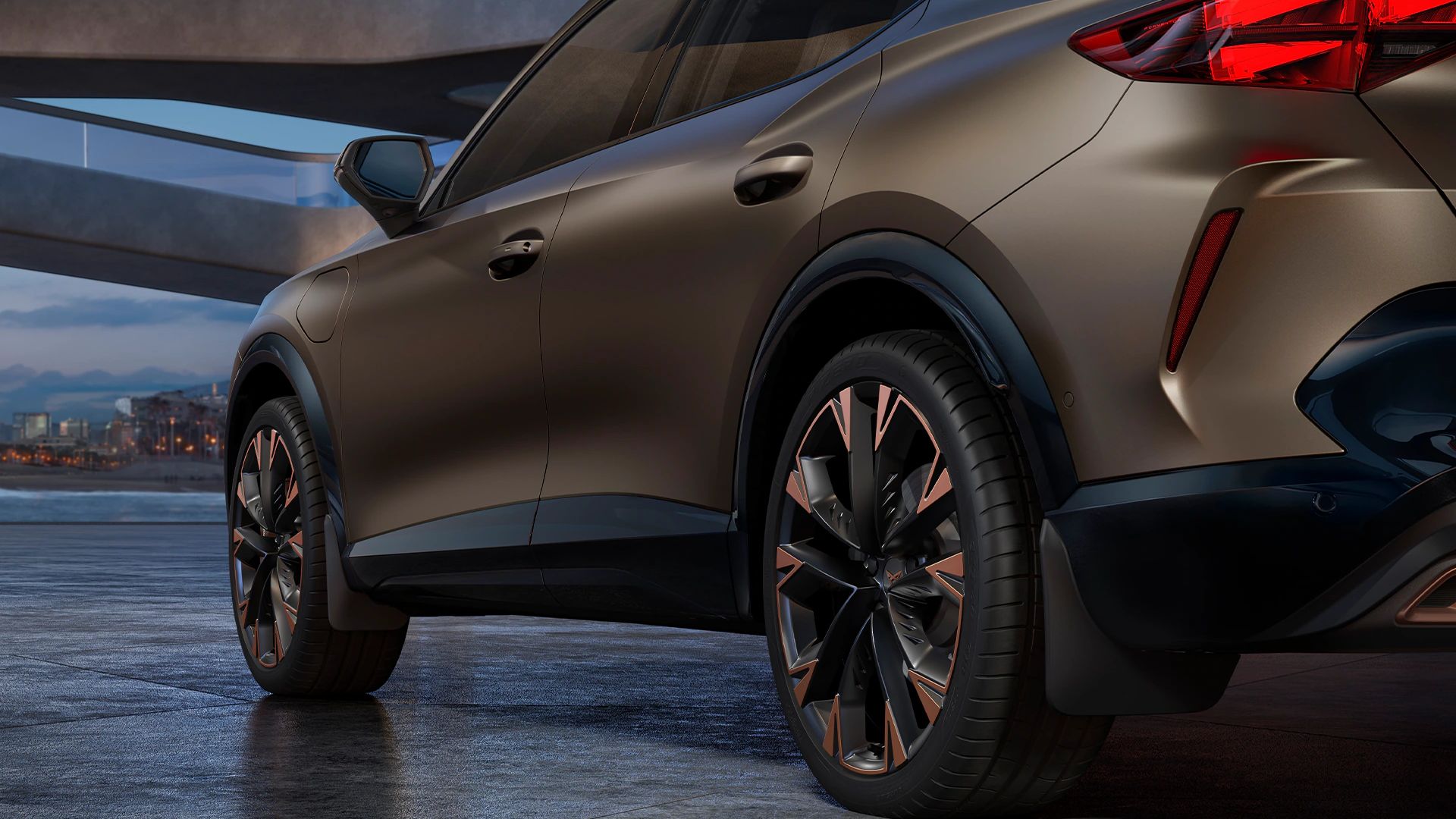 Ein CUPRA Formentor in einer Garage, mit Detailansicht auf die Hinterräder und Schmutzfänger. Das Fahrzeug ist in Bronze lackiert. Im Hintergrund sind architektonische Strukturen und eine Stadtlandschaft bei Dämmerung zu sehen.