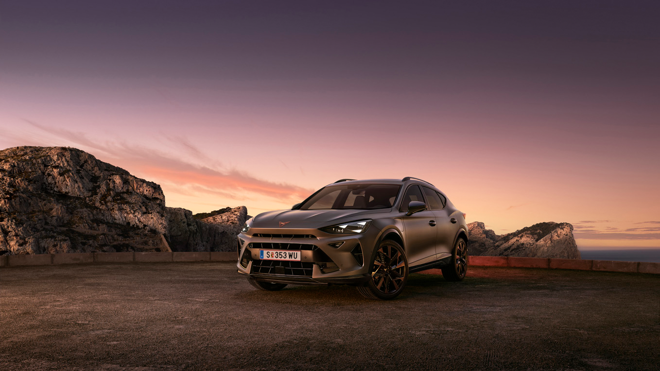 Ein grauer CUPRA Formentor parkt bei abendlicher Stimmung an einer Felsenküste.