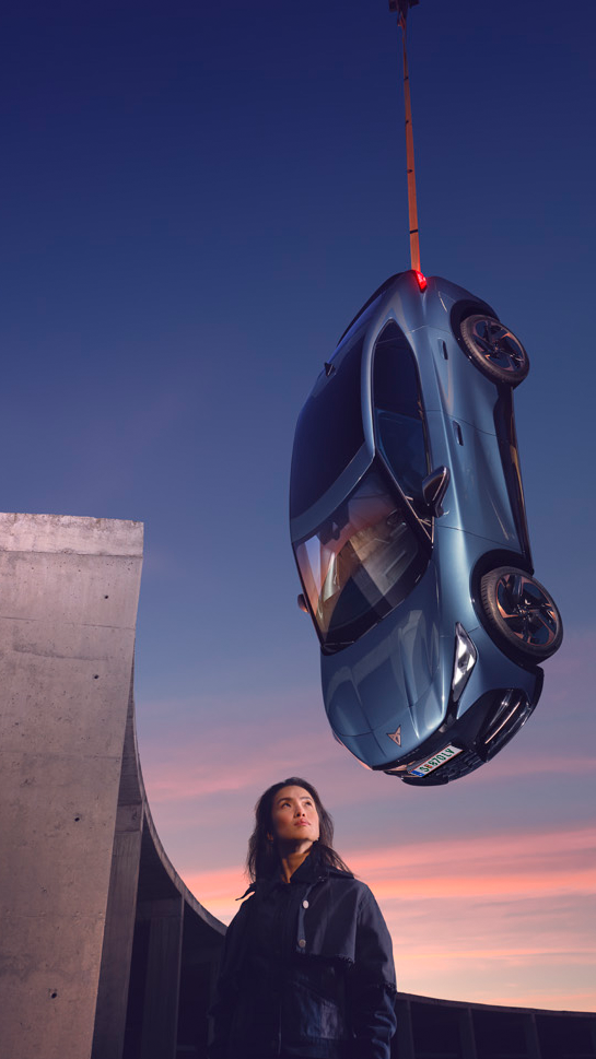 CUPRA Tavascan hängt an einem Seil vom Himmel. Eine Frau steht darunter.