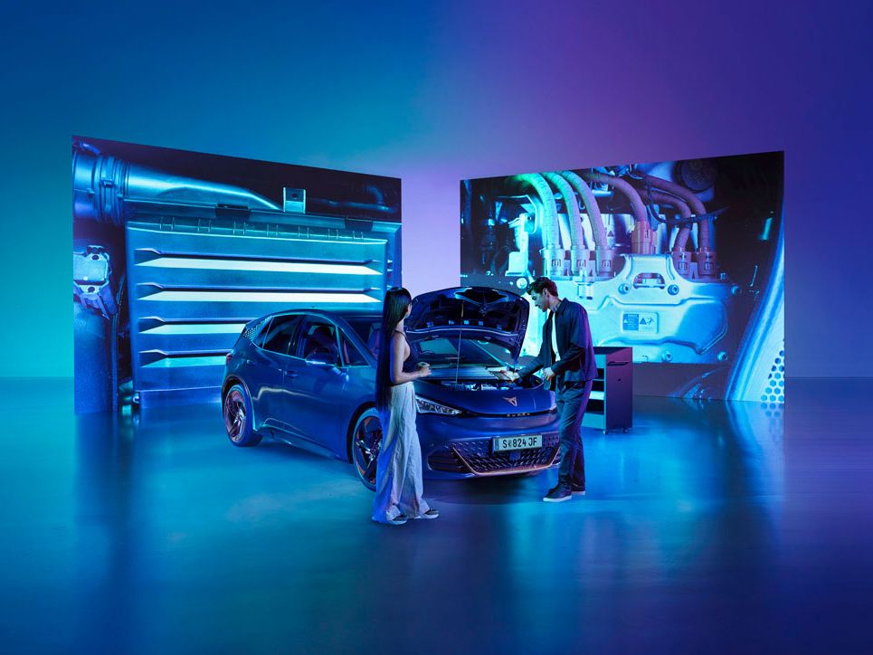 Eine Frau und ein Mann blicken bei geöffneter Kühlerhaube auf den Motor eines CUPRA Born