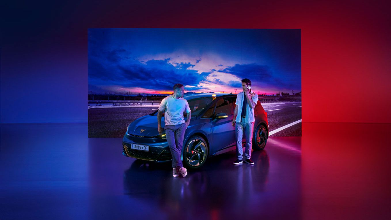 Ein Mann lehnt an einem CUPRA Born, ein anderer Mann steht daneben und telefoniert.