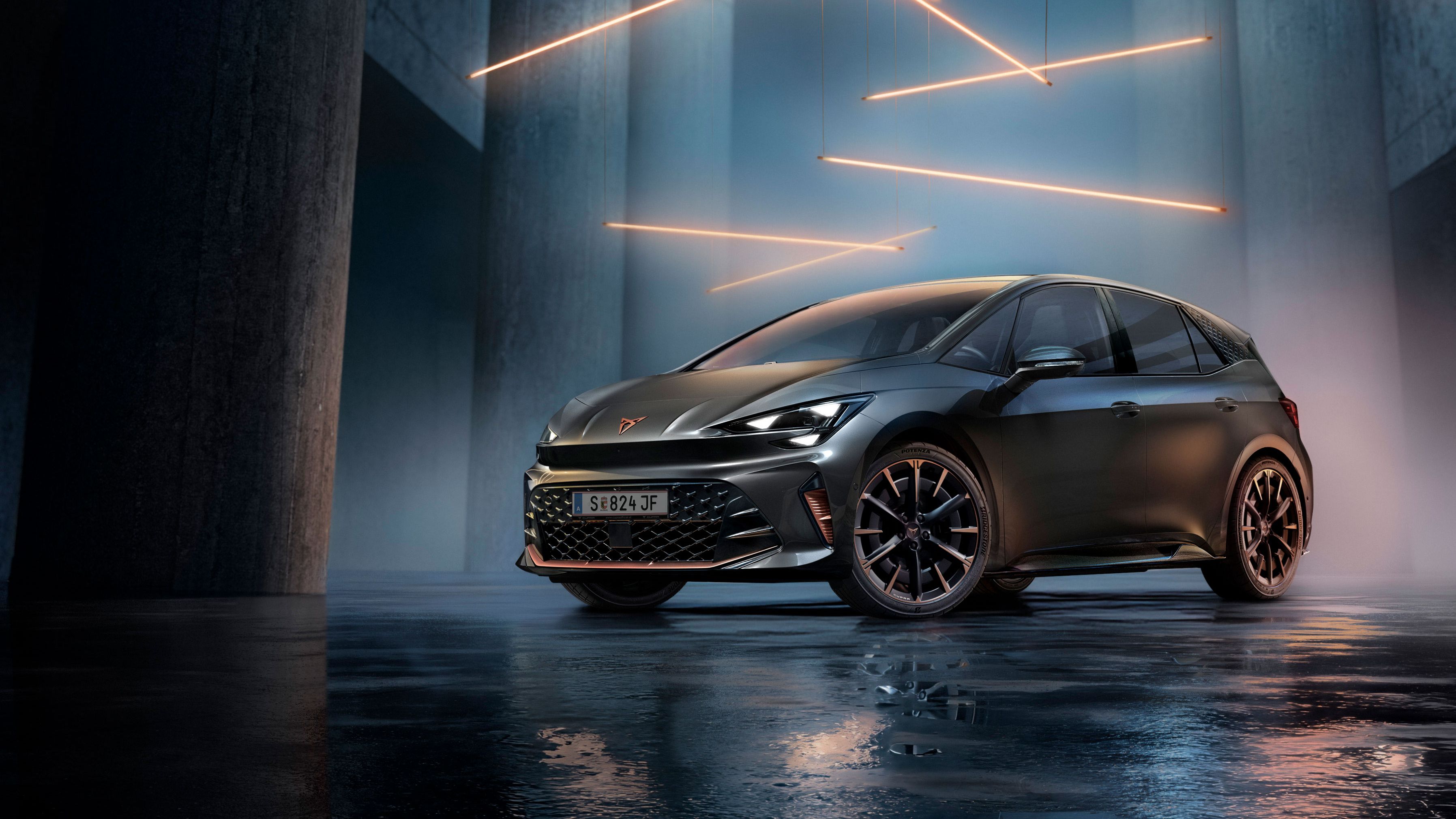 Ein grauer CUPRA Born steht in einer modernen, dunklen Umgebung mit vertikalen Säulen und leuchtenden LED-Streifen. Der Boden ist glänzend und reflektiert das Fahrzeug sowie die Beleuchtung. Das Auto wirkt kraftvoll und elegant.