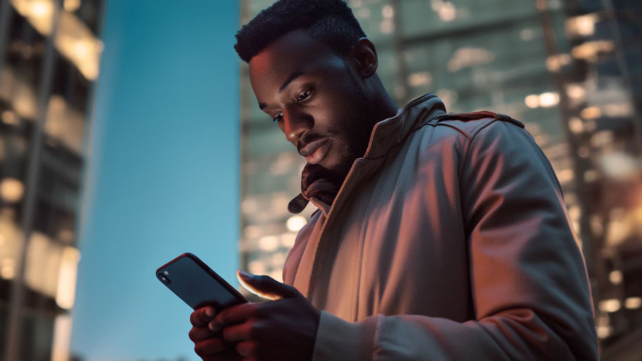 Ein Mann mit einem Smartphone in den Händen steht vor beleuchteten Gebäuden.