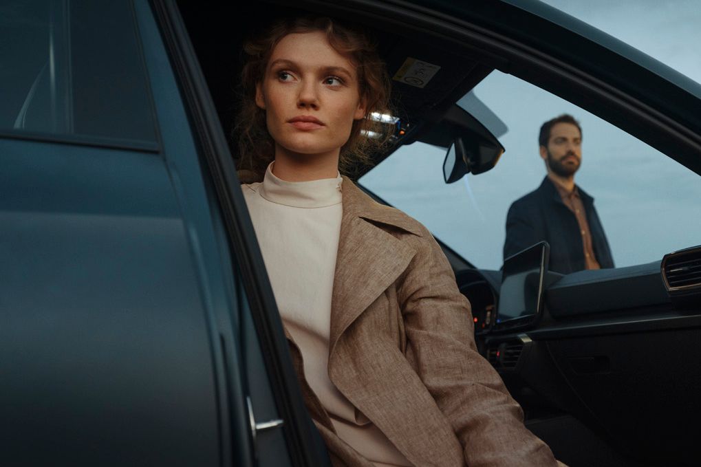 Eine Frau sitzt bei geöffneter Fahrzeugtür auf dem Beifahrersitz eines CUPRA Formentor. Im Hintergrund ist ein Mann zu sehen.