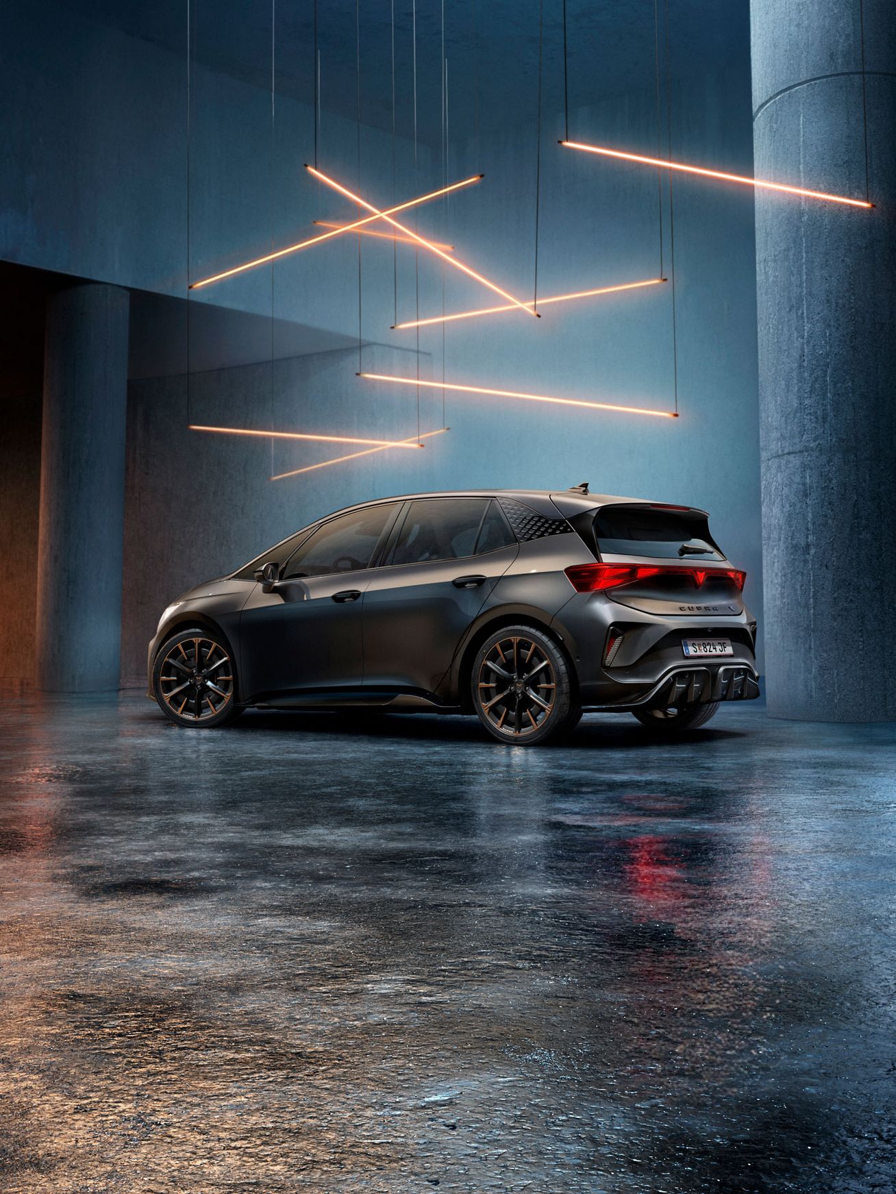 Ein CUPRA Born steht in einem stilvoll beleuchteten, industriellen Raum mit Betonwänden und -säulen. Von der Decke hängen mehrere lineare Lichtquellen, die ein elegantes Ambiente schaffen. Das Fahrzeug ist rückseitig zu sehen und reflektiert das Licht auf dem glänzenden Boden.