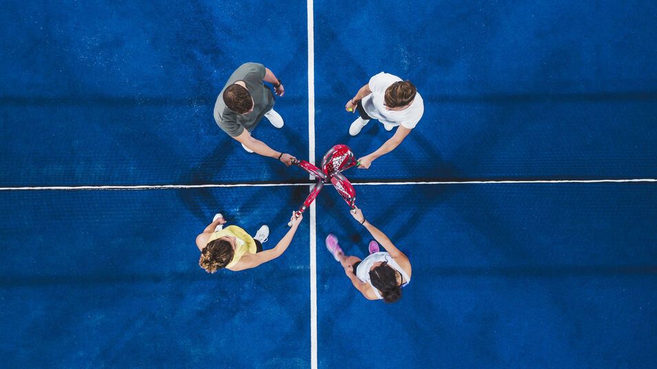 Blick von oben auf vier Sportler, die ihre Padels kreuzen.