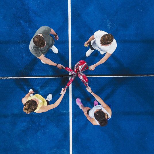 Blick von oben auf vier Sportler, die ihre Padels kreuzen.
