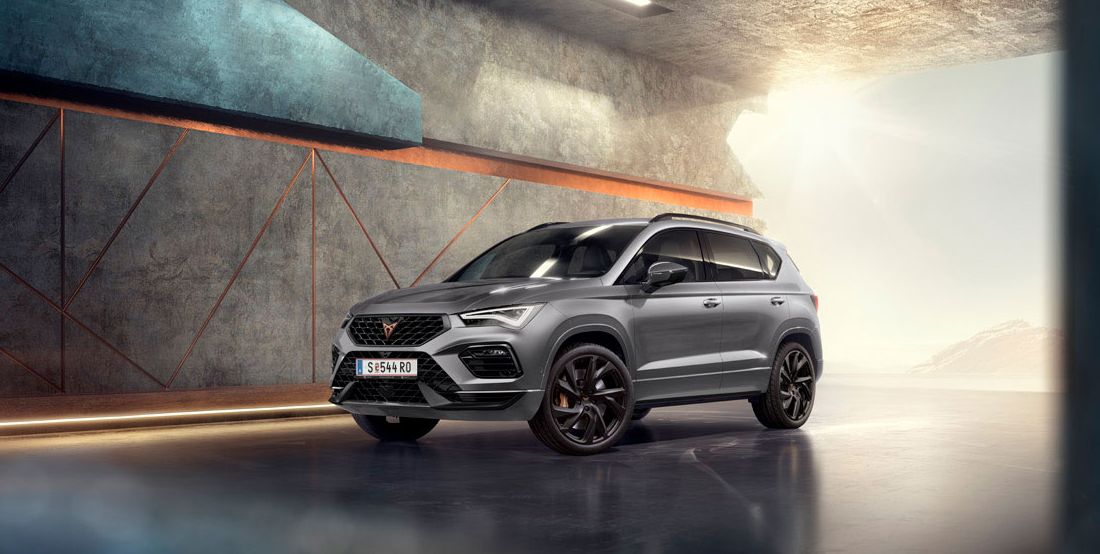 Ein CUPRA Ateca 2025 in Graphitgrau, ein sportliches und kompaktes SUV, geparkt in einer modernen, industriellen Umgebung.